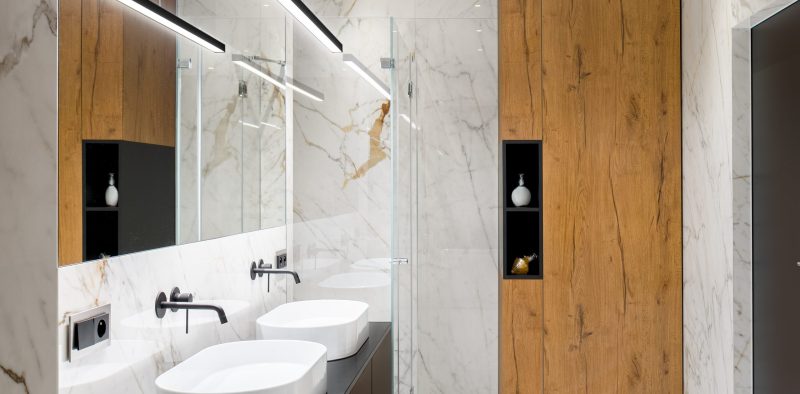 Luxury bathroom with marble tiles on floor and walls, two washbasins and wooden closet